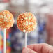 A hand holding a cake pop with Yum Crumbs Orange Creamsicle crumb topping on top.