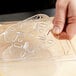 A hand holding a Vollrath clear polycarbonate drain tray over a counter.