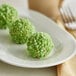A white plate with a close-up of a green pistachio crumb ball on it.