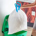 A woman's hand holding a white Hefty trash bag placing it in a green trash can.