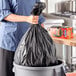 A woman holding a black Hefty garbage bag in a kitchen.