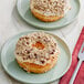 A plate with a donut topped with frosting and nuts next to a fork and knife on a red cloth.