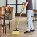 A person holding a yellow O-Cedar Commercial MaxiSweep angle broom.