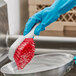 A person in blue gloves cleaning a pan with a red O-Cedar utility brush.