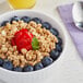 A bowl of Kellogg's Low-Fat Granola with blueberries and a strawberry on a white surface.