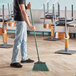 A man using an O-Cedar commercial angle broom with green bristles to sweep the floor.