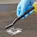 A hand in a blue glove using an O-Cedar stainless steel detail brush to clean a grill.