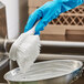 A person in blue gloves using an O-Cedar white nylon utility brush to clean a pan.