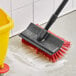 A red and yellow O-Cedar Commercial floor scrub brush head with squeegee on the floor.