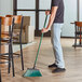 A person sweeping the floor with an O-Cedar Commercial green angle broom.