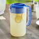 A Choice polypropylene beverage pitcher with lemonade and lemon slices on a white surface.