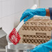 A person in blue gloves using a red and white O-Cedar utility brush to clean a silver pot.