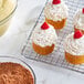 A tray of cupcakes with white frosting and raspberries on top sitting on a cooling rack.