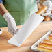 A person in white gloves holding a white insulated foil bread bag filled with a loaf of bread.