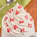 A cup with whipped cream and red and white Gertrude Hawk peppermint chunks.