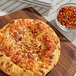 A pizza on a cutting board next to a bowl of Kari-Out Company crushed red chilies.