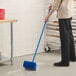 A person using a Lavex blue deck brush with a squeegee to sweep a floor.