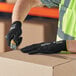 A person wearing Ansell HyFlex gloves with black nitrile palm coating using a tool to cut a piece of cardboard.