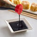 A Kari-Out Company soy sauce bottle pouring into a square white bowl of dark liquid.