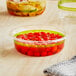 A World Centric compostable deli container filled with red tomatoes on a table.