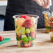 A clear 32 oz. compostable deli container filled with assorted fresh fruit pieces.