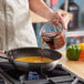 A person pouring brown liquid from a Kari-Out Company Sherry Cooking Wine bottle into a pan.