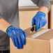 A person wearing  Ansell HyFlex blue gloves cutting a box with a knife.