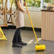 A woman using a yellow Laxex bi-level scrub brush to clean a floor.