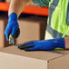 A person wearing blue Ansell HyFlex gloves and a safety vest cutting a box.