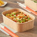 A rectangular Kraft paper take-out container with noodles and chopsticks inside.