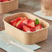 A rectangular Kraft paper take-out container filled with strawberries on a table.