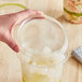 A hand holding a clear World Centric deli container with food and ice cubes.