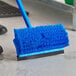 A blue Lavex brush head with long bristles and a squeegee on a floor.