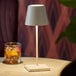 A Zafferano America Poldina Pro Mini white cordless table lamp on a table with a glass of whiskey and a cherry.