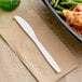 A white plastic Choice heavy weight polypropylene knife on a napkin next to a plate of food.