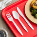 A red tray with a white plastic fork, knife, and spoon on a plate of food.