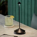 A Zafferano America black cordless table lamp on a table with a glass of lemonade and a lime.