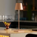 A Zafferano America Poldina Pro table lamp on a black counter with a drink and fruit.