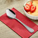 A Choice Milton stainless steel dinner spoon on a napkin next to a bowl of strawberries.