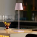 A Zafferano America Poldina Pro pink cordless table lamp on a black table with a drink and grapes.