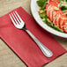 A Choice Milton stainless steel salad fork on a red napkin next to a plate of salad.