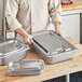 A man in a chef's uniform using a Vigor stainless steel steam table pan cover on a metal container.