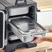 A person opening a Vigor stainless steel food container in an oven.