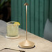 A Zafferano America gold table lamp lighting a table with a glass of lime juice.