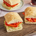 Sliced Bridor ciabatta baguette sandwiches with meat and sprouts on a cutting board.