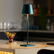 A Zafferano America Poldina Pro dark green cordless table lamp on a black and white table surface.
