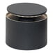 A dark gray cylinder with a round top on a table with lights.