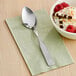 A Choice stainless steel medium weight dinner/dessert spoon in a bowl of ice cream with strawberries and sprinkles.
