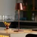 A Zafferano America Poldina Pro table lamp on a black counter top with a drink and fruit.