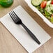 A black wrapped plastic fork on a white plate with a salad in it.